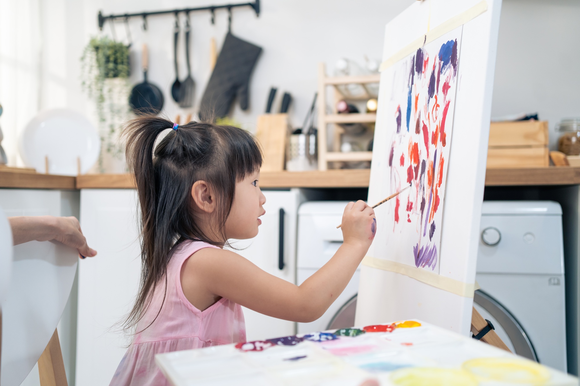 Asian young happy kid girl coloring on painting board in living room.