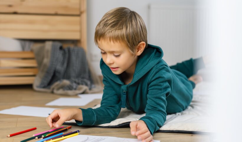 Boy drawing in on the floor a cozy room.