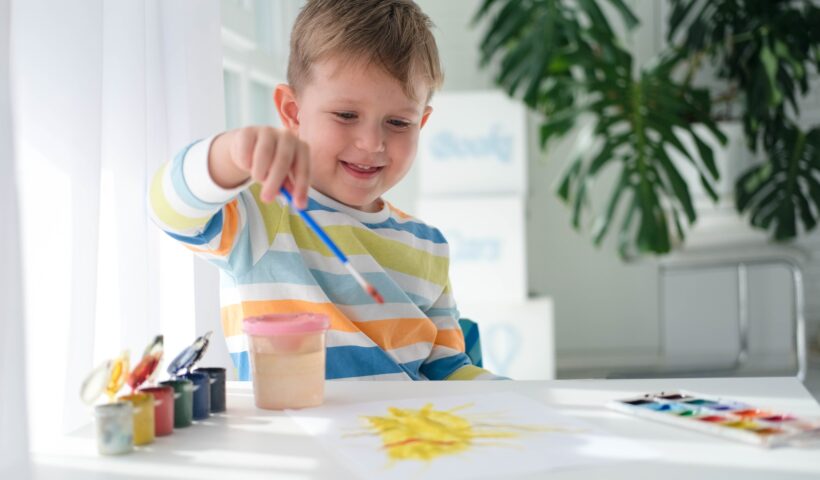 Happy kid painting with brush and colorful paints.