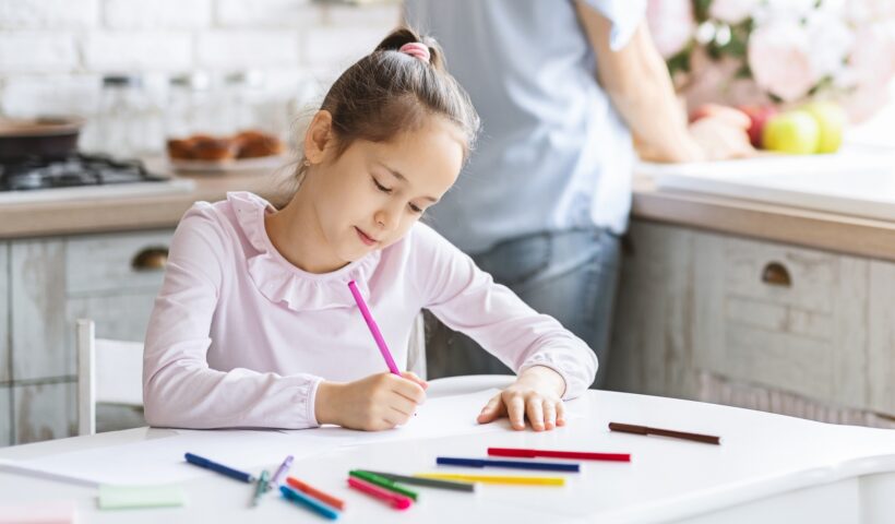Pretty little girl busy with drawing at kitchen table